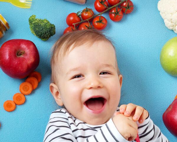 一个婴儿躺在蓝色的背景上，周围是各种水果和蔬菜。