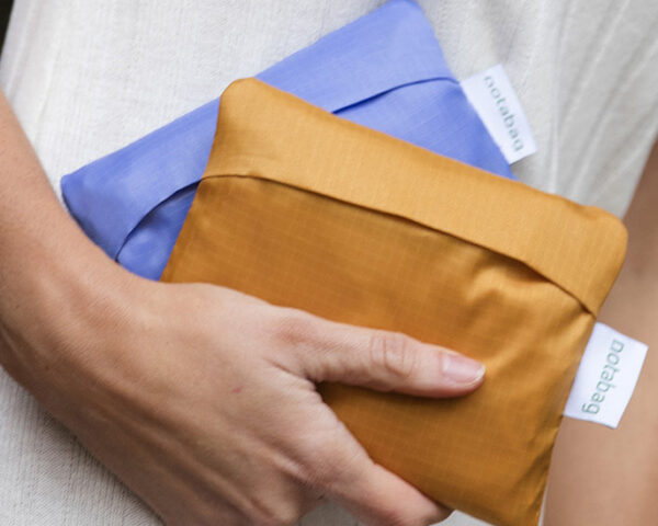 一只手拿着两个手提包折叠成长方形，一个紫色，一个橙色