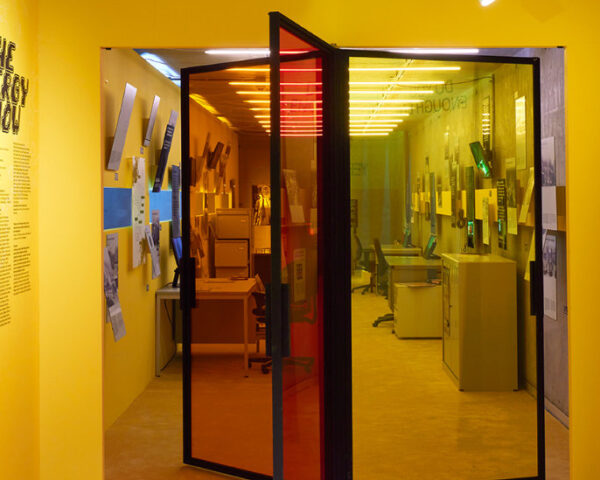 黄色墙壁的空间，中心有一个玻璃旋转门，通往一个展览