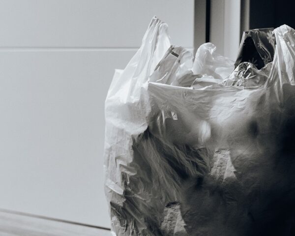 一张黑白照片，一个装满塑料瓶的塑料袋坐在门口